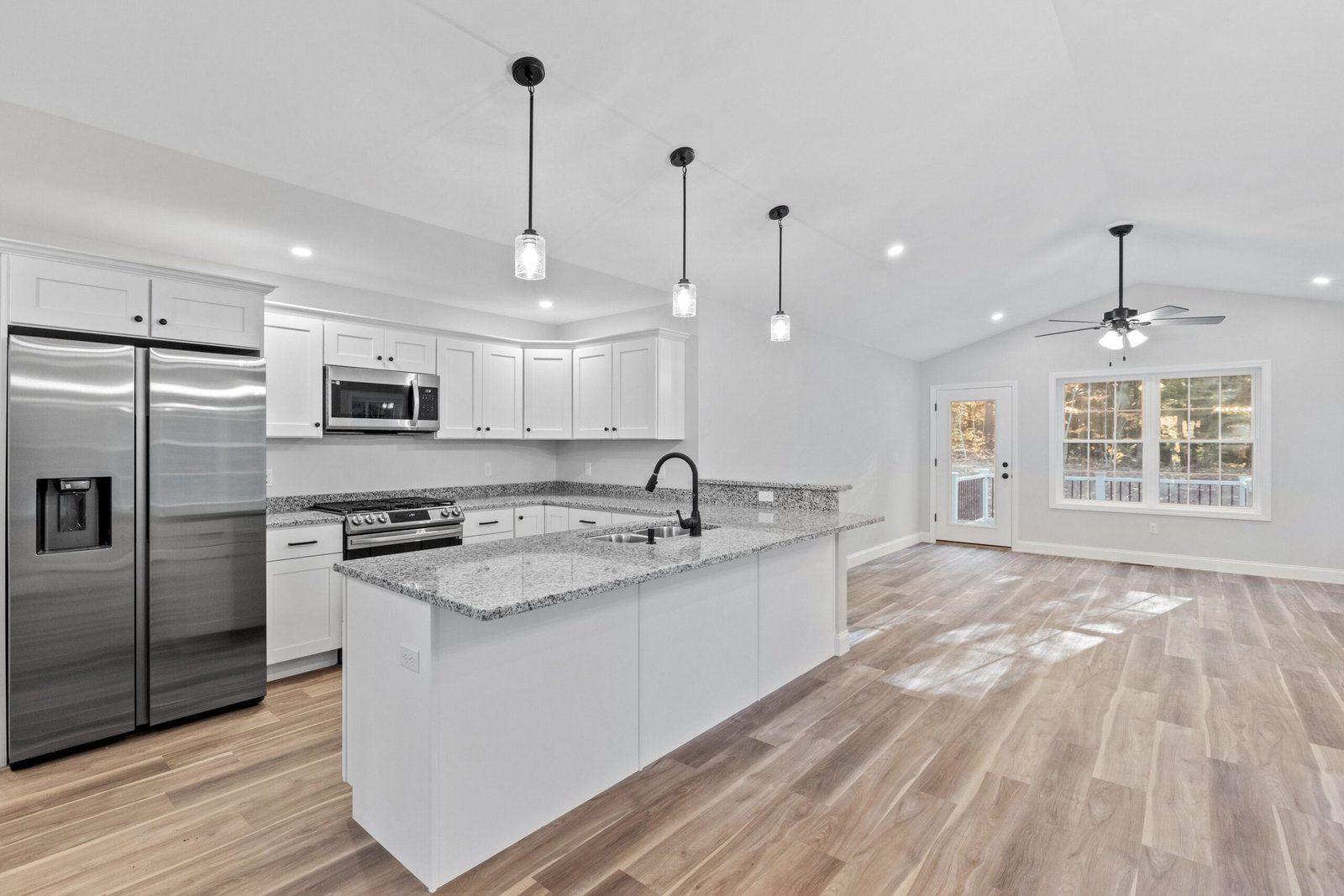 A newly renovated kitchen with hardwood floors, white furniture, silver appliances and a marble island